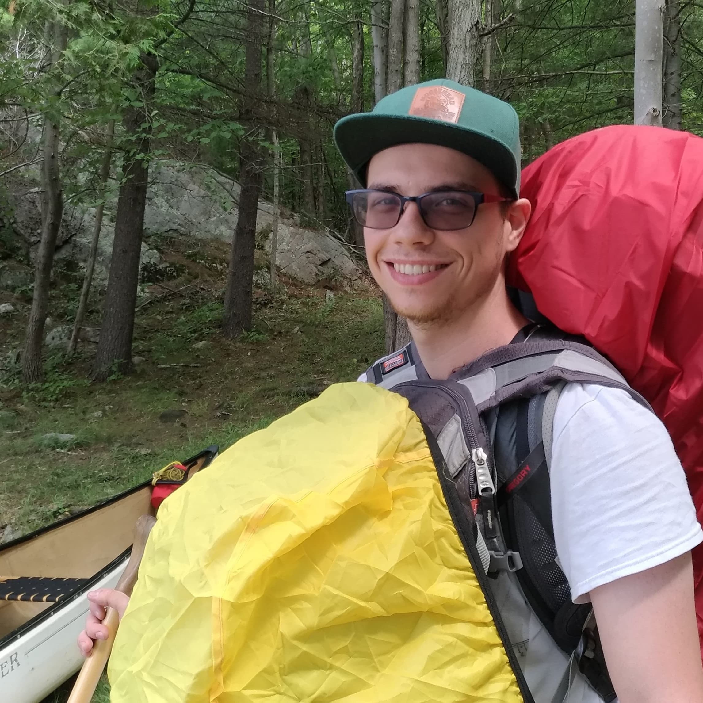 Paul with red and yellow backpacks next to a canoe in the forest