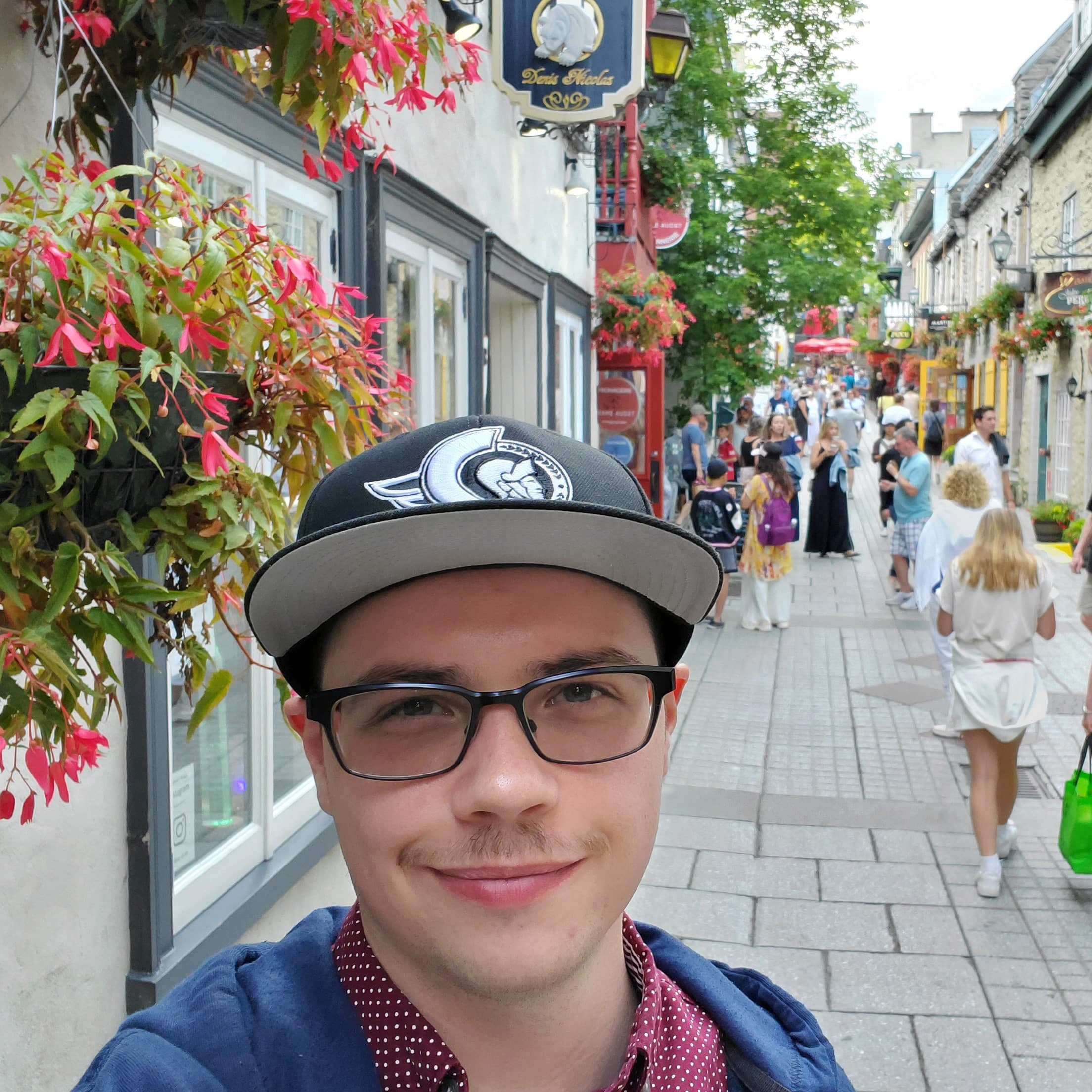 Paul selfie with old Quebec City buildings and colourful hanging flowers and cobblestone roads in background